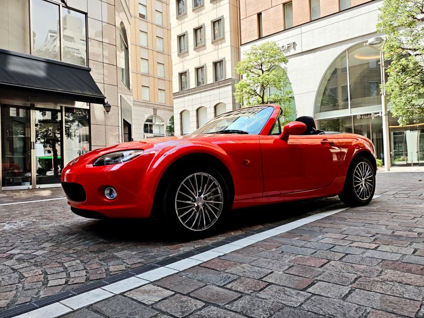 A vibrant red convertible parked on a cobblestone street in a city with tall buildings.